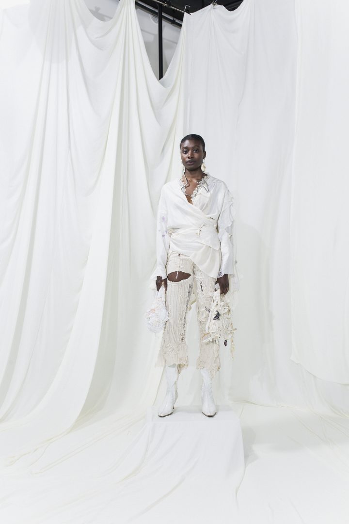 Model is wearing a white wrap shirt andoff-white striped trousers. On both hands they carry white bags
