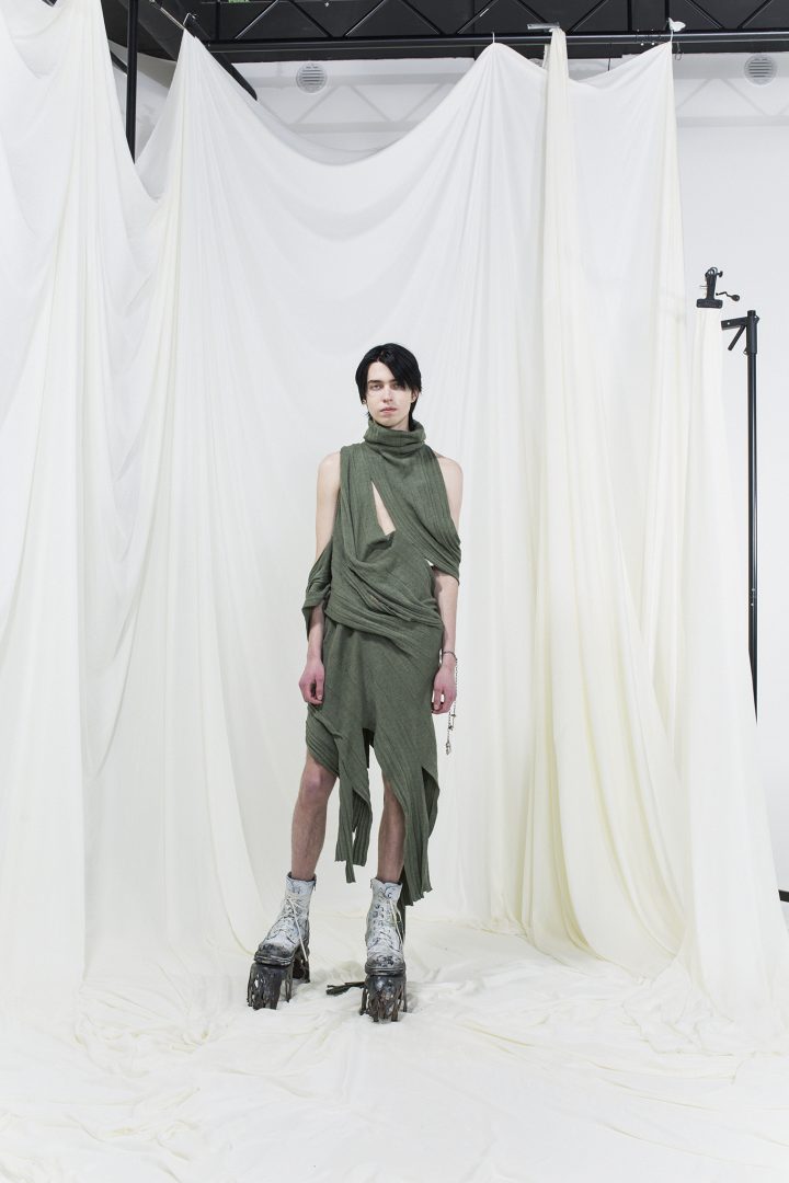 Model wearing sage green draped knitted dress with white boots