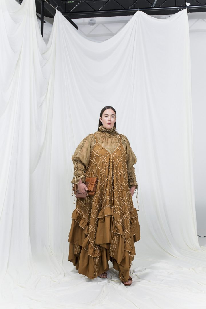 Model is wearing a toffee-brown modular silk dress with sheer matching top underneath