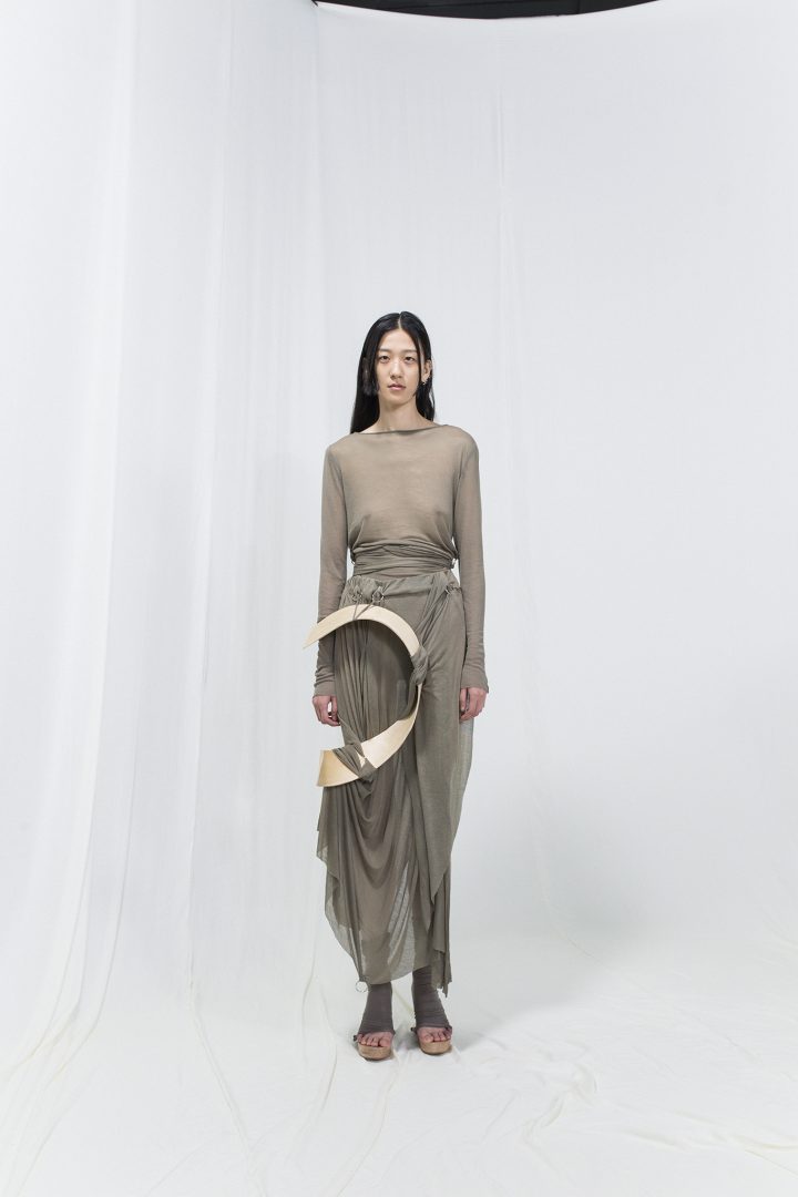 Model wearing a grey jersey dress with bended birch piece attached