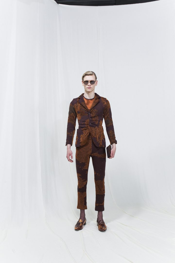 Model is wearing a printed brown blazer with gatherings and matching cropped trousers. Sunglasses and brown wallet as accessories