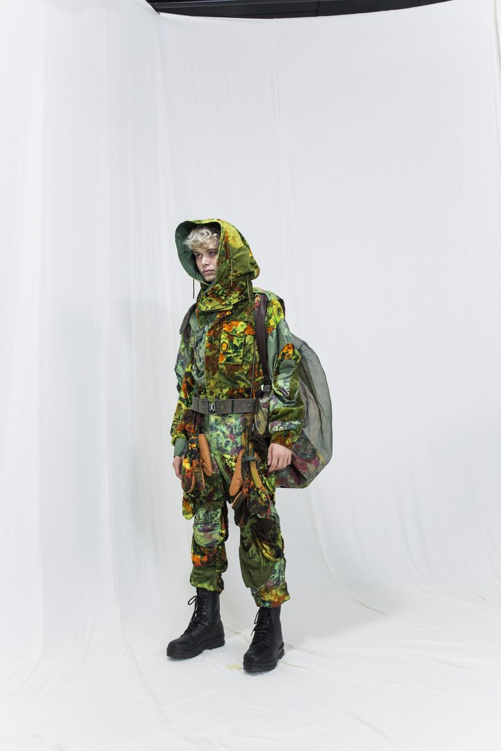 Model is wearing a multicoloured floral jacket with matching pants and a hood, see through rucksack